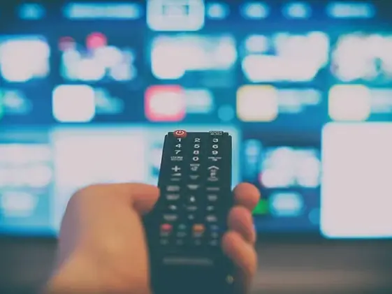 Mão segurando o controle remoto diante da TV
